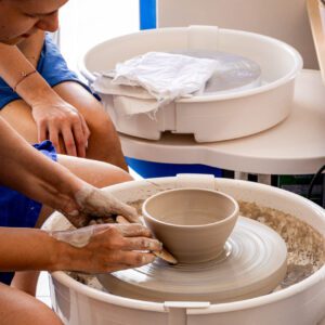 kobieta toczy na kole garncarskim miskę, warsztaty ceramiczne "rozkręć się"