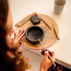 Kobieta lepi miseczkę z czarnej gliny