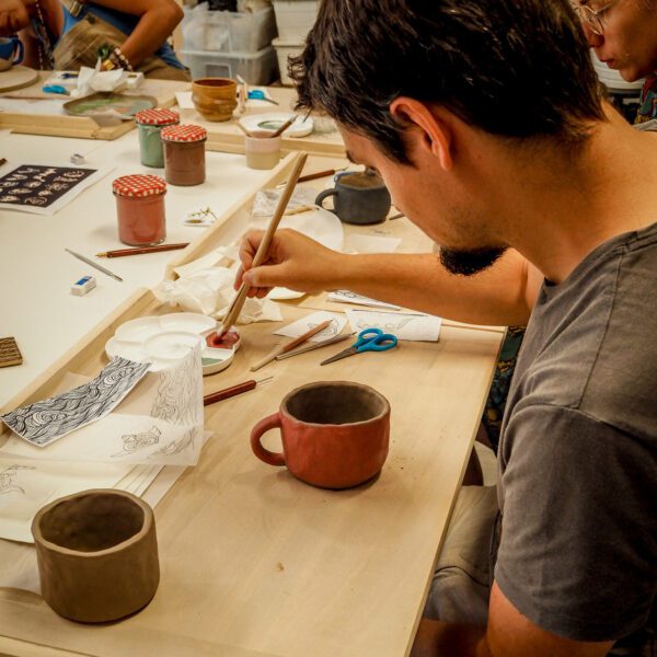mężczyzna maluje gliniany kubek lepiony ręcznie na warsztatach ceramicznych