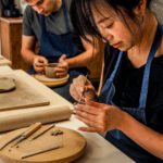 poranki-z-gliną Kobieta lepi małe puzzle z gliny, w tle mężczyzna formuje ceramiczną miskę