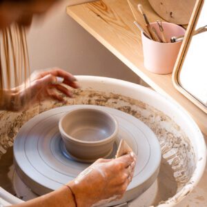 Kobieta toczy na kole garncarskim niewielką miskę z gliny