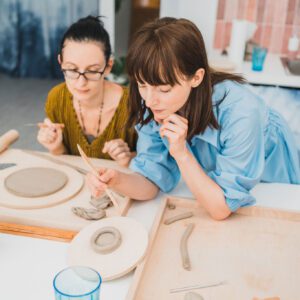 Nauczycielka ceramiki pokazuje uczennicy jak poprawnie lepić z gliny