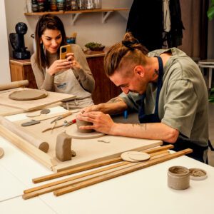 kobieta robi zdjęcie mężczyźnie, który lepi z gliny gliniany kubek